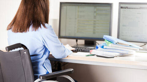 Frau im Rollstuhl sitzt am PC und arbeitet