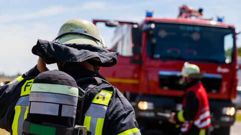 Ein Feuerwehrmann im Einsatz mit Auto im Hintergrund