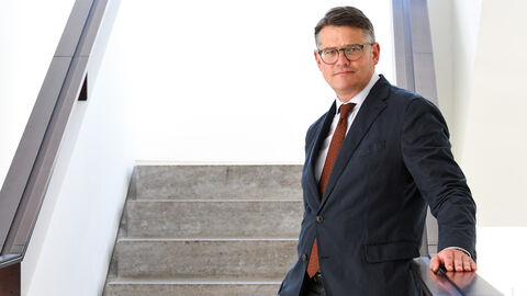 Boris Rhein steht auf einer Treppe, an das Treppengeländer angelehnt.