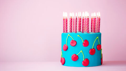 Eine blaue Geburtstagstorte mit Gummikirschen und vielen pinken Kerzen