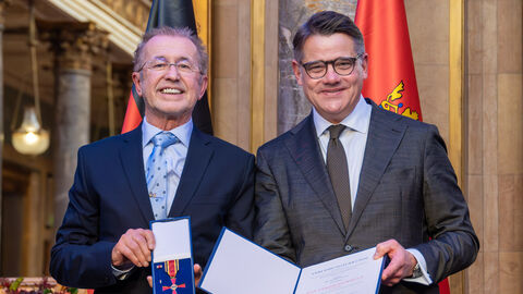 Zwei Personen stehen nebeneinander und halten die Auszeichnung hoch.