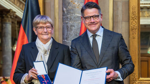 Zwei Personen stehen nebeneinander und halten die Auszeichnung hoch.