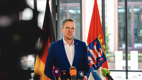 Christoph Degen, Staatssekretär im Hessischen Ministerium für Wissenschaft und Forschung, steht vor Mikrofonen in einer Interviewsituation.