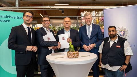 Innenminister Poseck und weitere Personen stehen um einen Stehtisch herum und halten die Kooperationsvereinbarung in Händen.