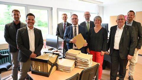 Wissenschaftsminister Timon Gremmels mit weiteren Personen stehen hinter einem Tisch mit Papierakten 